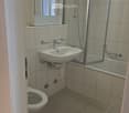 Modern bathroom, white tile, toilet, sink, shower, bathtub, glass wall, mirror