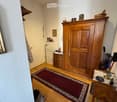 Entrance hall with wooden floor, white walls, wooden cabinet, red rug, white door, wooden desk, umbrellas, shoes, and a picture frame on the wall.