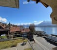 View from balcony of a village with houses, a road, a lake, and mountains in the background