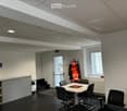 Office space with a round table, chairs, coffee machine, coat rack, and shelves.