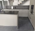 modern kitchen, white cabinets, black countertops, stainless steel sink, black tiled floor, built-in oven, open staircase