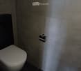 Bathroom: white toilet, gray tiled wall, black tiled floor, silver toilet paper holder
