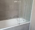 Bathtub with glass door, silver faucets, tiled walls, tiled floor
