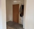 Empty room with wooden door, tiled floor, white walls, bench, clothes hanging on a rack