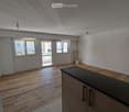 Empty room with wooden floor, white walls, large windows, sliding door, radiator, kitchen counter