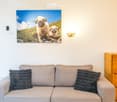 A living room with a gray couch, two pillows, a wooden cabinet, a wall-mounted photo, and a wall lamp.