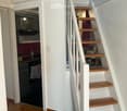 white walls, wooden floor, white staircase, kitchen with black appliances, open door to another room