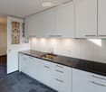 modern kitchen with white cabinets, black countertops, stainless steel sink, faucet, electrical outlets, and a window with decorative glass