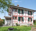 2 story house, red and white exterior, green shutters, covered patio, garden, outdoor seating