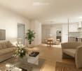 Modern living room with beige couch, glass coffee table, and a round chair. A potted plant and a lamp are on the side table. A dining area with a table and chairs is visible in the background. The kitchen is equipped with white cabinets, a microwave, and