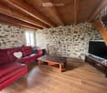 Living room with exposed wooden beams, stone walls, red leather sofa, wooden coffee table, and TV on a stand.