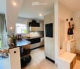 Modern kitchen with white tiled floor, black and white cabinets, a central island, and a blackboard. A mixer, flowers, and books are on the island. A mirror and a handbag are on the wall.