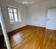 Empty room with wooden floor, white walls, large window, and a door.