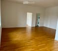 empty room, wooden floor, white walls, two doors, one leading to a laundry room with a washing machine