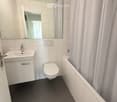 Modern bathroom with white tiles, a sink, toilet, bathtub, and a large mirror above the sink.