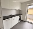 Modern kitchen with white cabinets, black countertop, stainless steel sink, and built-in oven. Features a large window with a view of the balcony.