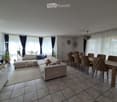 Furnished Room. Open-plan living and dining area with a sectional sofa, coffee table, dining table with chairs, and large windows with curtains.