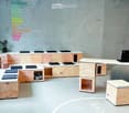 Furnished Room. Modern, minimalist workspace with wooden desks, cabinets, a laptop, and a small plant on a shelf.