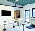 Furnished Room. Modern office space with white tables, laptop, stools, a large screen, a ball chair, and a treadmill.