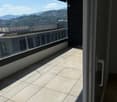 Spacious balcony with tiled floor, large glass sliding doors, and a scenic view of mountains and cityscape.