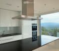 Kitchen. Modern kitchen with white cabinets, black countertops, stainless steel appliances, and expansive windows offering a scenic view.