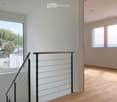 Corridor / Hallway. Modern hallway with wooden flooring, white walls, large windows, and a staircase with a metal railing leading to another room.