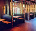 Restaurant interior with wooden tables, benches, and hanging lamps, featuring birch tree trunks as decorative columns.
