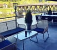 Outdoor terrace with wicker furniture, glass table, and scenic view of a river and bridge.