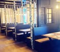 Restaurant interior with wooden tables, benches, and chairs arranged around birch tree trunks, warm lighting, and wooden flooring.