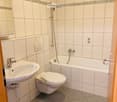 Bathroom. Modern bathroom with white tiles, a sink, toilet, bathtub, and a mirror. Features a handheld showerhead and a decorative border on the wall tiles.