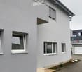 House. Modern two-story house with light gray exterior, multiple windows, and a small garden area with a paved walkway.