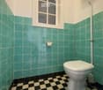 Bathroom with green tile walls, black and white checkered floor tiles, a toilet, and a window