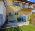 Garden / Outdoor Area. Garden area with green artificial grass, patio furniture including chairs and a table, a staircase leading to a balcony, and a small potted plant.