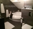 Bathroom. Modern bathroom with a corner bathtub, toilet, towel racks, and a large mirror. The space features dark tiles and a skylight window.