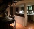 Furnished Room. A modern, open-plan living and dining area with a sleek dining table and chairs, a small kitchen counter, and built-in cabinets. The space features warm wooden flooring and ambient lighting.