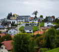 House. A residential neighborhood with multiple houses, featuring varied architectural styles, green lawns, and trees.