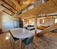 Furnished Room. Open-plan living and dining area with wooden beams, a round dining table with chairs, a sofa, a bed, and a fireplace.