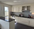 Modern kitchen with white cabinets, dark granite countertops, and stainless steel appliances including a microwave, coffee maker, and teapot. Features a central island and built-in lighting.