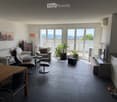 Modern living room with large windows, grey sofa, armchair, coffee table, floor lamp, and cat furniture.