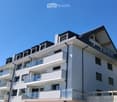 Modern multi-story residential building with white facade, multiple balconies, and a flat roof with small dormer windows.