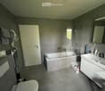 Modern bathroom with a bathtub, sink, toilet, mirror, and cabinet. Features grey tiles, a glass shower enclosure, and a towel rack with towels.