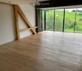Unfurnished Room. Empty room with wooden beams, wooden floor, and large glass windows leading to a balcony with a view of a green landscape.