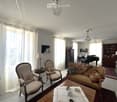 Elegant living room with a cream-colored sofa, wooden coffee table, armchairs, a grand piano, and bookshelves.