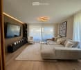 Modern living room with a large sectional sofa, armchair, coffee table, TV mounted on a wooden wall, and decorative picture frames on a black console table.