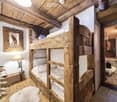 Cozy bedroom with wooden bunk bed, table lamp, framed picture, and a small sitting area with a sofa and rug.