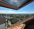 View from a rooftop terrace showing a cityscape with houses, trees, and a clear blue sky.