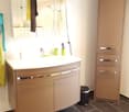 Modern bathroom with a white sink, mirror, and beige cabinets. Includes a towel, cups, and a trash bin on the floor.