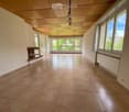 Empty room with tiled floor, large windows, fireplace, and wooden ceiling.