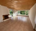Empty room with tiled floor, fireplace, large windows, and sliding glass doors leading to a garden.