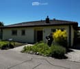 Single-story house with beige walls, dark roof, small garden, and driveway.